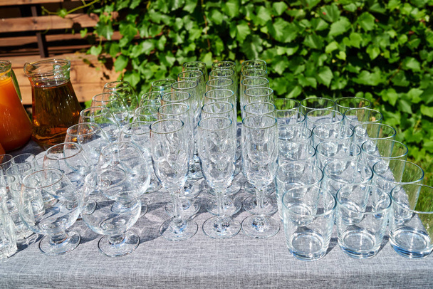 Rows of empty glasses on table outdoors, free space. Set of sparkling glassware. Crystal glasses ready for celebration on table. Wineglasses at luxury wedding reception outside - Foto, Imagen