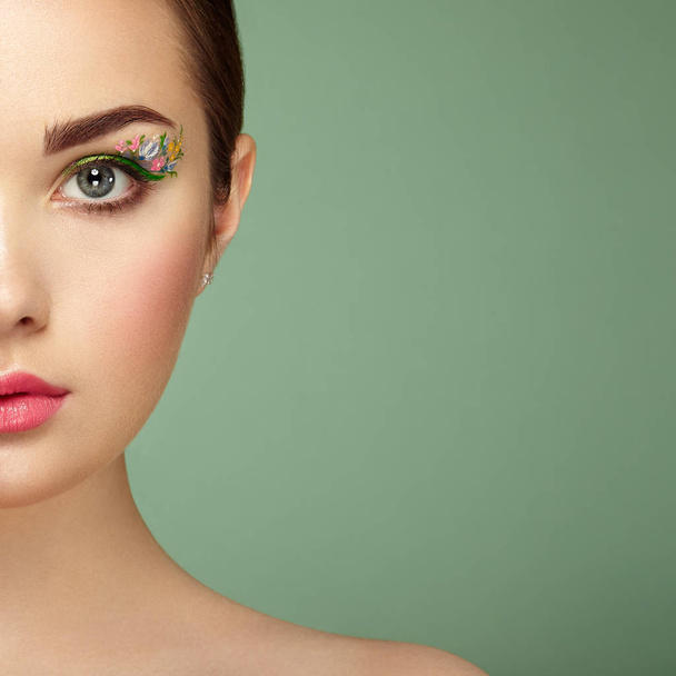 Young beautiful woman with flower makeup eyes. Spring makeup. Beauty fashion. Eyelashes. Cosmetic Eyeshadow. Make-up detail. Girl on green background - Foto, Imagem