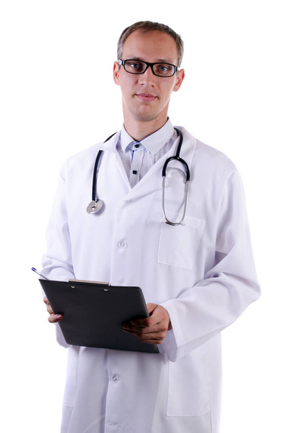 A doctor in a white coat with a stethoscope and wearing glasses holds a folder for writing on an isolated background - Foto, Imagen