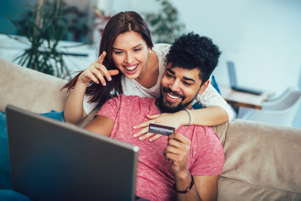 Mies käyttää kannettavaa tietokonetta ja nainen, jolla luottokortti kotona, käsite ostoksia verkossa
 - Valokuva, kuva