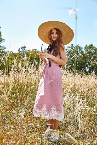 Beautiful young sexy woman long hair bright makeup nature background landscape dry spike grass and trees garden summer model dressed in cotton dress accessory straw hat sunglasses fashion style. - Foto, Bild