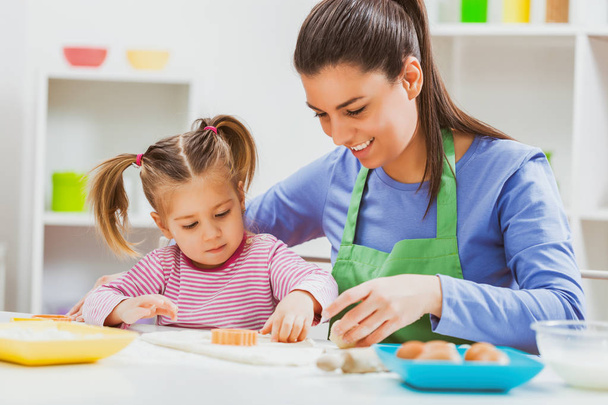 Happy mother and daughter are making cookies in their kitchen.  - Foto, imagen