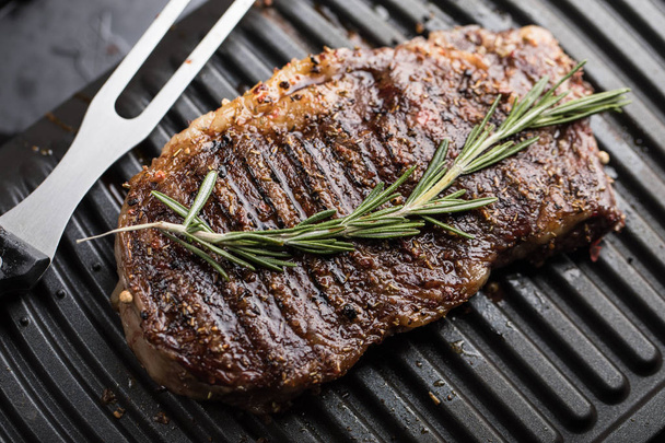 Steak meat with rosemary leaves on grill grid - Foto, imagen