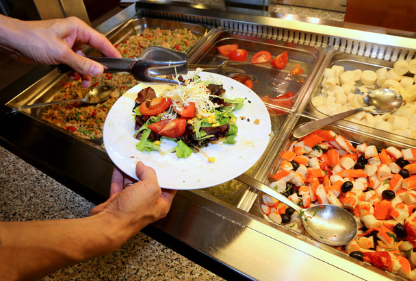 mão do caixeiro durante a pausa para o almoço que enche o prato com legumes frescos na cantina da empresa
 - Foto, Imagem