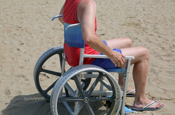 człowiek z tank top i spodenki na wózku inwalidzkim na piaszczystej plaży latem - Zdjęcie, obraz
