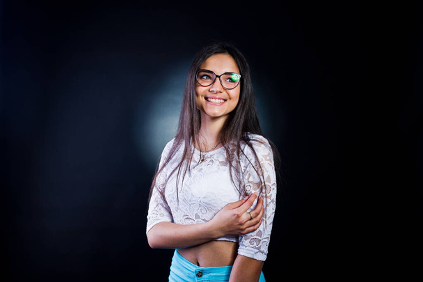 Portrait of an attractive young woman in white top and blue pants posing with her glasses in the dark. - Foto, afbeelding