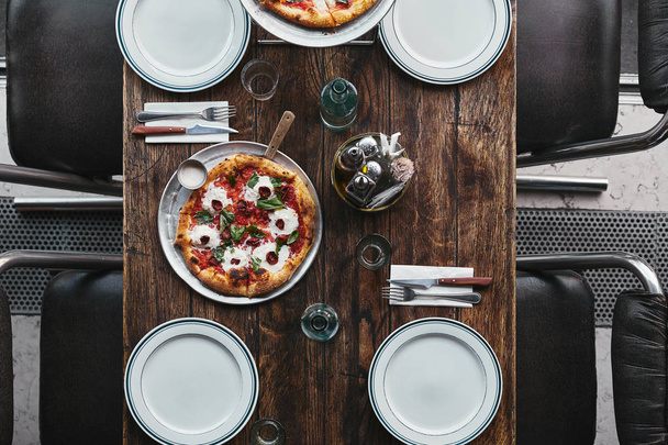 top view of tasty pizza margherita on tray and plates on rustic table at restaurant - Φωτογραφία, εικόνα