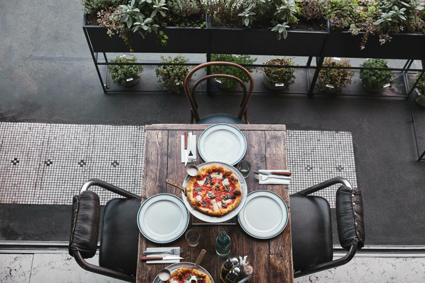 top view of tasty pizza margherita on tray and table setting at restaurant - Фото, изображение