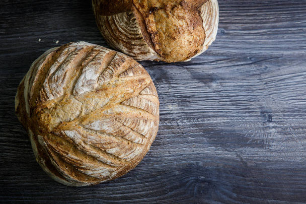 two tasty whole handmade round white wheat bread lie on  dark wooden table - Foto, Imagem