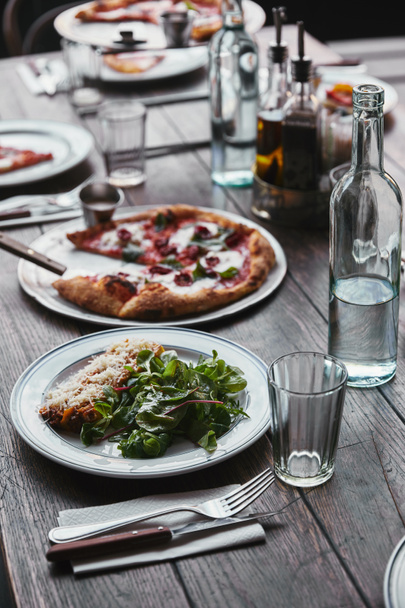 Detailní záběr vynikající pizzu a lasagne na dřevěný stůl s vodou - Fotografie, Obrázek