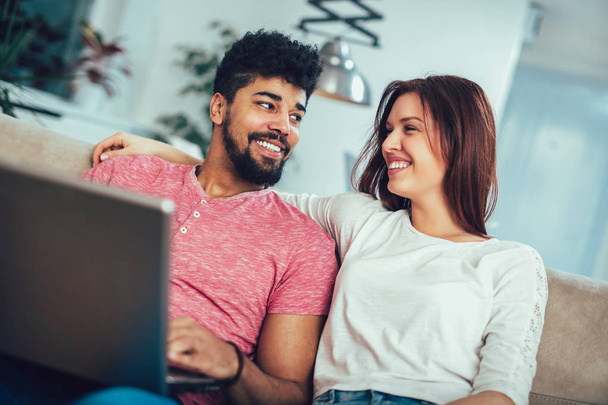 glückliches junges Paar sitzt zu Hause mit Laptop auf dem Sofa  - Foto, Bild