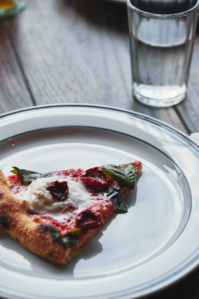 close-up shot of tasty pizza margherita on white plate with glass of water - Фото, изображение
