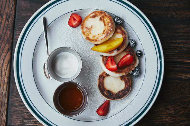 top view of delicious cheese pancakes with bowls of dippings on wooden table - Photo, Image