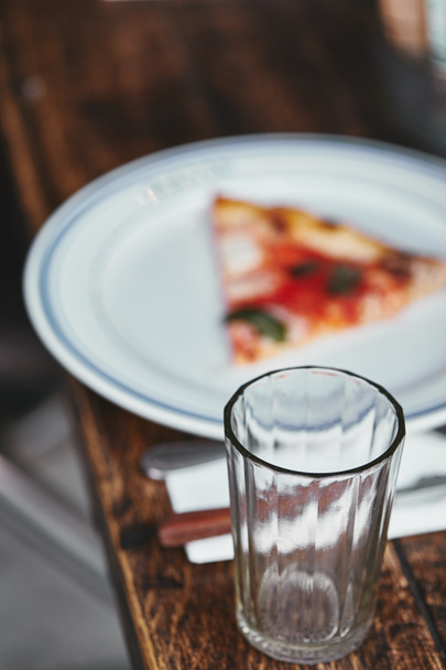 close-up shot of drinking glass with blurred slice of pizza on plate - Фото, изображение