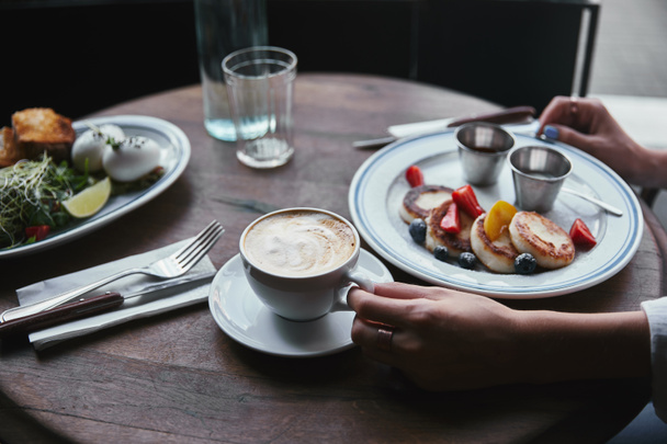 oříznutý snímek ženy s tvarohem palačinky, salát a kávu na dřevěný stůl v restauraci - Fotografie, Obrázek