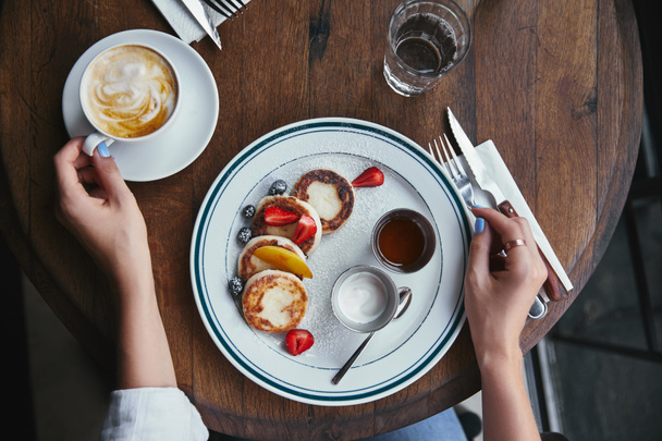 tiro recortado de mujer con delicioso syrniki y café en la mesa rústica en el restaurante
 - Foto, imagen