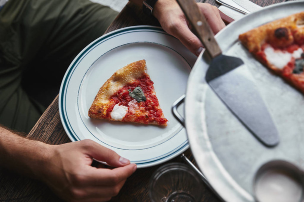bijgesneden schot van man eten heerlijke pizza margherita in restaurant - Foto, afbeelding