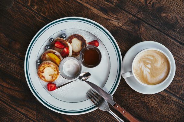 вид сверху на вкусные сироники на тарелке и чашку кофе на деревенском деревянном столе
 - Фото, изображение