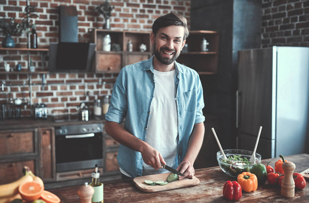 Handsome man is cooking on kitchen and smiling. - Foto, Bild