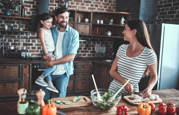Mom, dad and daughter are cooking on kitchen. Happy family concept. Handsome man, attractive young woman and their cute little daughter are making salad together. Healthy lifestyle. - Zdjęcie, obraz