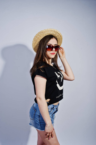 Portrait of an attractive girl in black t-shirt saying lol, denim shorts, hat and sunglasses posing in the studio. - Foto, Imagem
