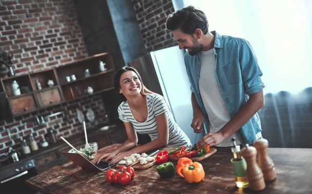 Romantic couple is cooking on kitchen. Handsome man and attractive young woman are having fun together while making salad. Healthy lifestyle concept. - Foto, afbeelding