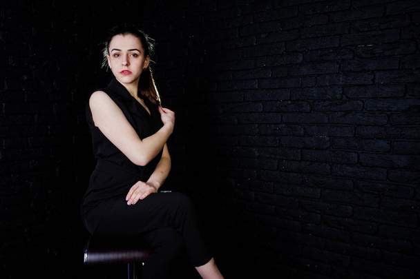 Portrait of a beautiful brunette girl in black jumpsuit sitting and posing in the studio. - Photo, Image