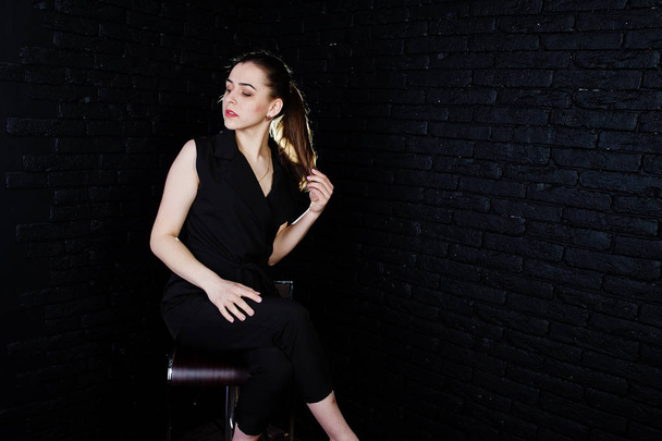 Portrait of a beautiful brunette girl in black jumpsuit sitting and posing in the studio. - Fotoğraf, Görsel