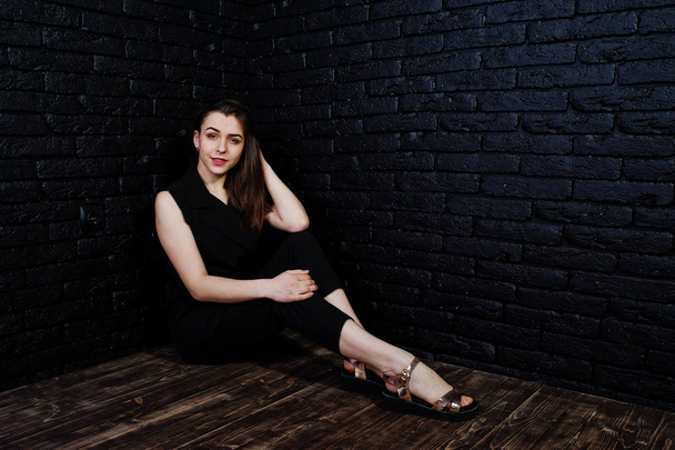 Portrait of a beautiful brunette girl in black jumpsuit sitting and posing in the studio. - Foto, imagen