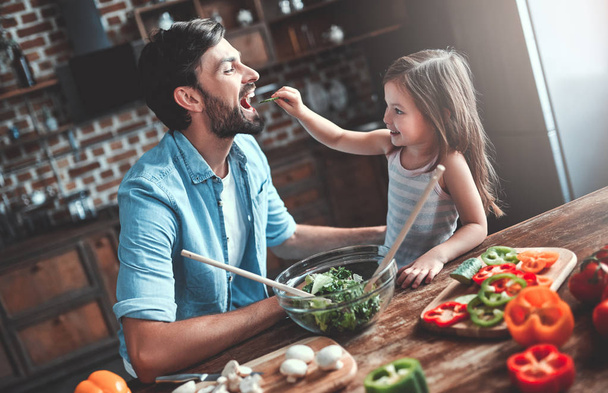 Handsome man and his little cute daughter are cooking on kitchen. Making salad. Healthy lifestyle concept. - Photo, Image