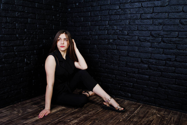Portrait of a beautiful brunette girl in black jumpsuit sitting and posing in the studio. - 写真・画像