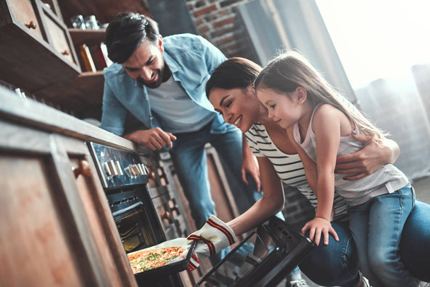 Mom, dad and daughter are cooking on kitchen. Happy family concept. Handsome man, attractive young woman and their cute little daughter are making pizza together. - Фото, зображення