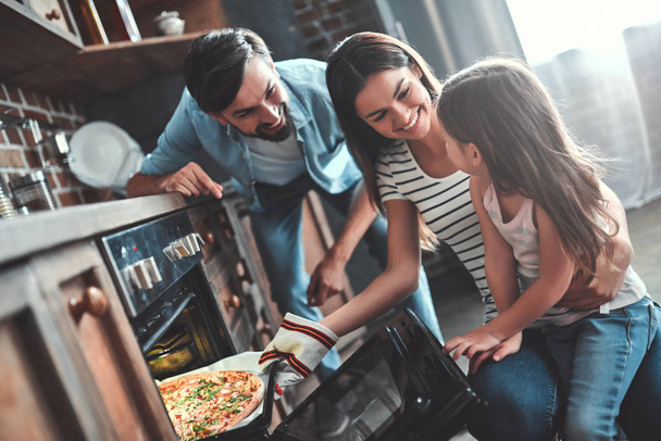 Mom, dad and daughter are cooking on kitchen. Happy family concept. Handsome man, attractive young woman and their cute little daughter are making pizza together. - Foto, imagen