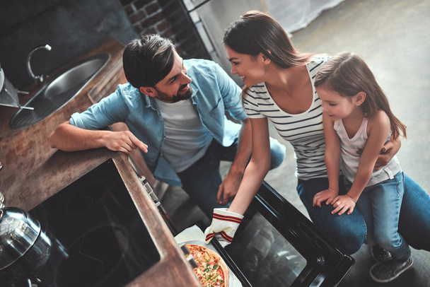 Mom, dad and daughter are cooking on kitchen. Happy family concept. Handsome man, attractive young woman and their cute little daughter are making pizza together. - Valokuva, kuva