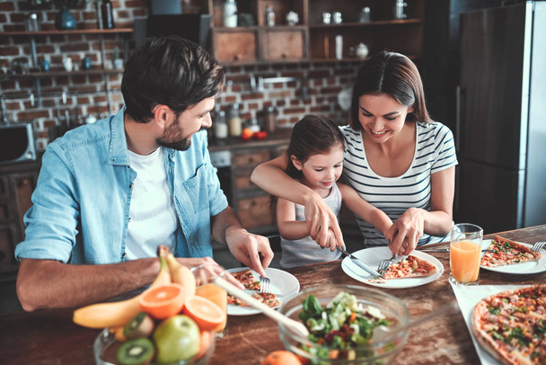 Mom, dad and daughter are eating together on kitchen. Happy family concept. - Фото, изображение