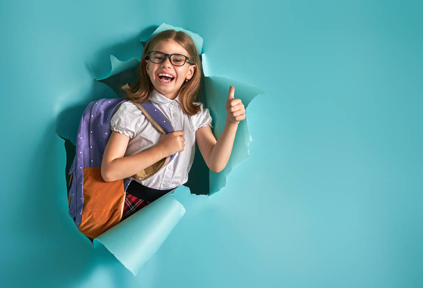 Back to school and happy time! Cute industrious child is breaking through color paper wall. Kid with backpack. Girl ready to study. - Foto, immagini