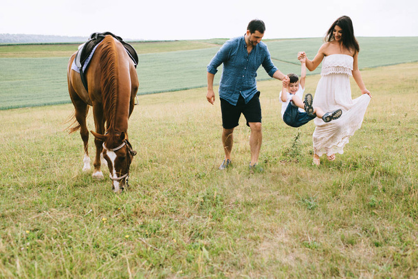 family holding hands and walking near horse on field  - Φωτογραφία, εικόνα