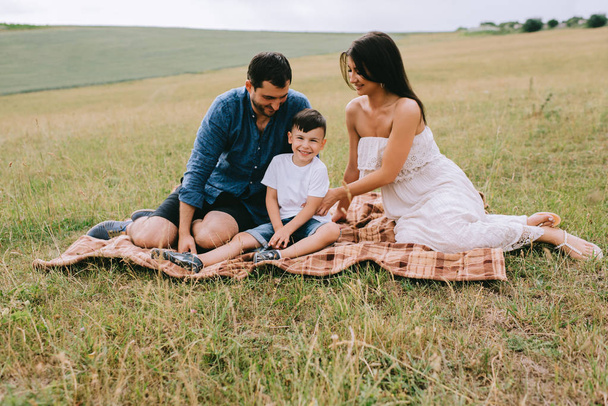 щасливі батьки і син сидять на ковдрі на полі
 - Фото, зображення