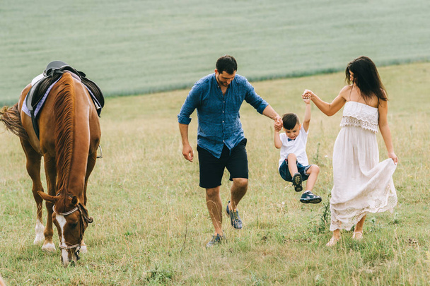 rodzice i syn, trzymając się za ręce i zabawy w pobliżu konia na pole - Zdjęcie, obraz