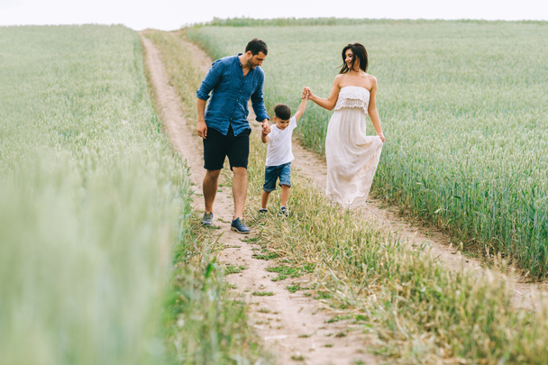 parents and son holding hands and walking on path in green field - Foto, afbeelding