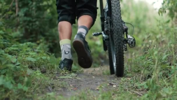 male cyclist comes with bicycle on trail, close up - Materiał filmowy, wideo