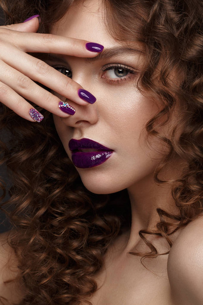 Beautiful girl with evening make-up, purple lips, curls and design manicure nails. beauty face. - Фото, изображение