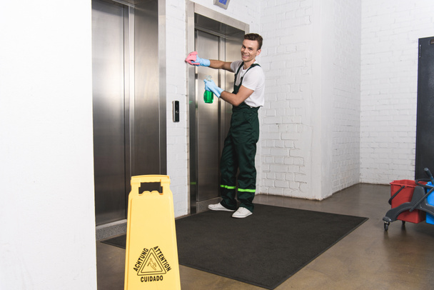 красивый молодой уборщик убирает лифт и улыбается в камеру
  - Фото, изображение