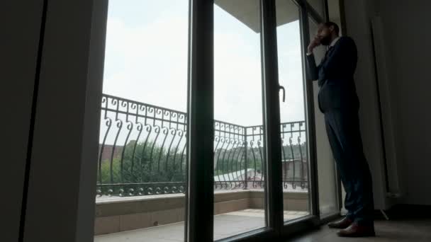 Γεμάτο σώμα σιλουέτα ενός επιχειρηματία στέκεται και κοιτάζει έξω από το σφάλμα των windows στο γραφείο του - Πλάνα, βίντεο