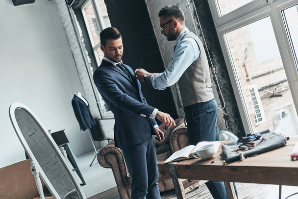 fashionable designer adjusting jacket on his client in boutique workshop with mannequin and mirror  - Φωτογραφία, εικόνα