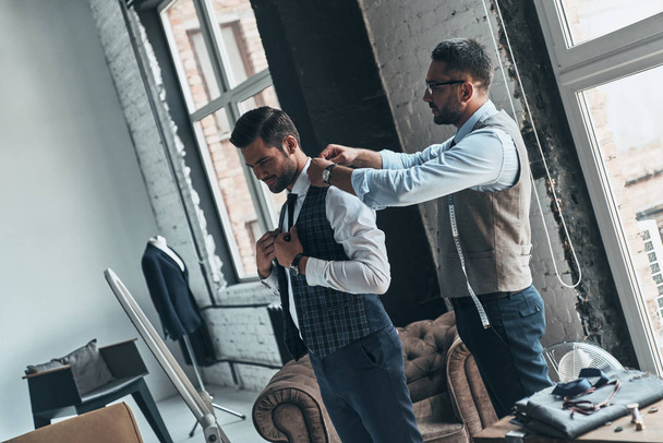 fashionable man choosing suit with help of fashion designer in boutique - Foto, afbeelding