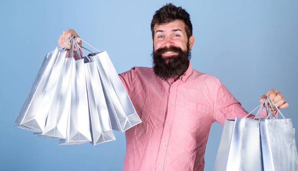 Sale and discount concept. Guy shopping on sales season with discounts. Hipster on happy face is shopping addicted or shopaholic. Man with beard and mustache hold shopping bags, light blue background - Foto, Bild