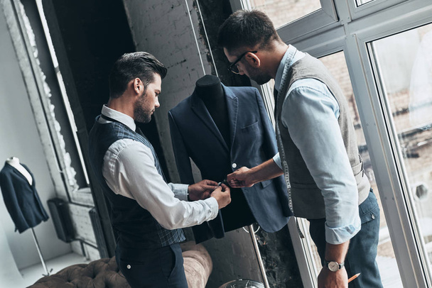 two young fashionable men standing in workshop and working on jacket details  - Photo, image