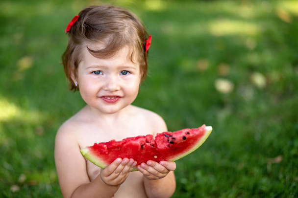 Τα παιδιά τρώνε φρούτα σε εξωτερικούς χώρους. Υγιεινό σνακ για τα παιδιά. Κοριτσάκι παίζει στον κήπο κρατώντας μια φέτα καρπούζι. Το παιδί τρώει καρπούζι στον κήπο. - Φωτογραφία, εικόνα