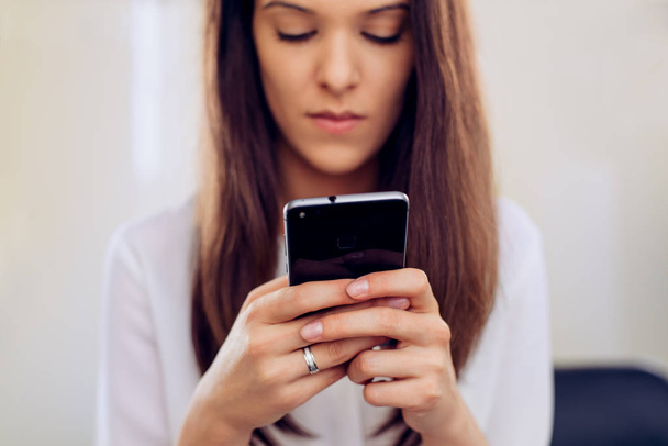 Mujer de negocios en su oficina con mensajes de texto para teléfonos inteligentes
 - Foto, Imagen